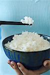 Woman holding bowl of rice and chopstick, close up