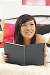 Girl lying on bed, holding diary, looking away