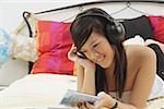 Girl lying on bed, holding CD case, listening to headphones