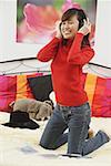 Girl in bedroom, kneeling on bed, listening to headphones