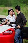 Couple with red sports car, arguing