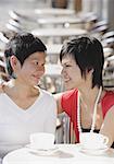 Mother and adult daughter in cafe smiling at each other