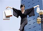 Woman dressed in black, arms outstretched, carrying shopping bags