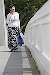 Mature woman carrying shopping bags, walking along bridge