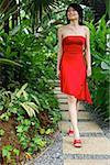 Femme vêtue d'une robe rouge, marchant le long de l'allée de jardin