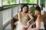 Two young women sitting on patio, smiling at camera