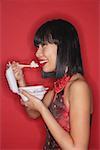 Woman standing red background, eating rice from a Styrofoam container