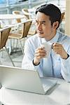 Businessman in cafe with laptop, holding mug, looking away