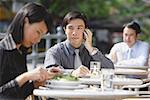 Business people at outdoor café, focus on man with mobile phone