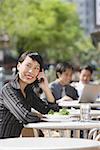 Businesswoman using mobile phone at outdoor cafe, people in the background