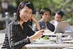 Femme d'affaires à l'aide de téléphone portable au café en plein air, messagerie textuelle, souriant à la caméra