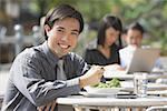 Businessman having lunch at outdoor cafe, smiling at camera