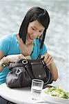 Jeune femme assise au bord de la rivière café, regardant dans son sac à main