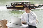 Businessman sitting at outdoor cafe, using laptop, river in the background