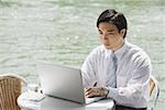 Businessman at outdoor cafe, using laptop, river in the background