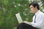 Businessman sitting in park with laptop, side view