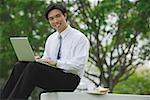 Businessman sitting in park with laptop, looking at camera