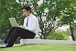 Young businessman sitting in park using laptop