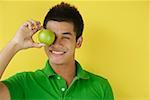 Man holding green apple over eyes smiling at camera