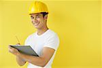 Man wearing hardhat, writing on clipboard, smiling at camera