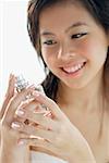 Young woman looking at perfume bottle, smiling