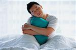 Man sitting in bed, embracing pillow