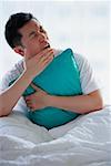 Man sitting in bed, embracing pillow, yawning