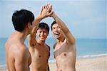 Three men on beach, putting hands together