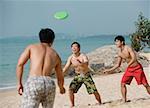 Three young men on beach playing with Frisbee