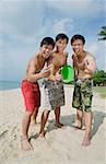 Three men on beach, standing side by side, making hand sign