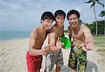 Men on beach, standing side by side, making hand sign