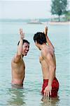 Two men standing in sea, giving high fives