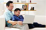 Father and son in living room, looking at laptop