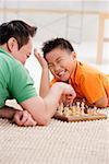 Father and son lying on floor, playing chess, son laughing