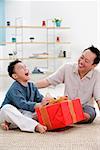 Father and son at home, boy opening gift, looking up