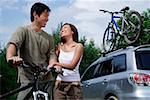 Mann auf dem Fahrrad, Frau stand neben ihm, Sports Utility Vehicle im Hintergrund
