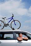 Man sitting in car, leaning out of window, bicycle on the roof of car