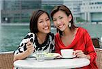 Deux femmes au café trottoir déjeunant, souriant à la caméra