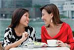 Two women at sidewalk cafe having lunch, smiling at each other