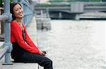 Woman sitting by river, listening to MP3 player, smiling at camera