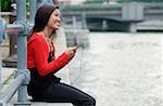 Woman sitting by river, listening to MP3 player