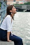 Woman sitting by river, smiling, looking up