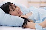 Jeune femme allongée sur le lit, souriant à la caméra