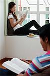 Woman sitting on bay window reading a book, man in foreground reading