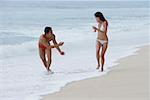 Couple running along beach, man splashing woman with water