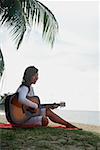 Young woman sitting on beach playing a guitar