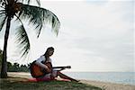 Young woman sitting on beach with a guitar