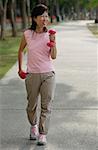 Mature woman using dumbbells, walking along path