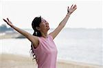 Woman standing on beach, looking up, arms outstretched