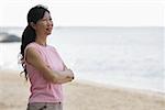 Woman standing on beach, arms crossed, looking away